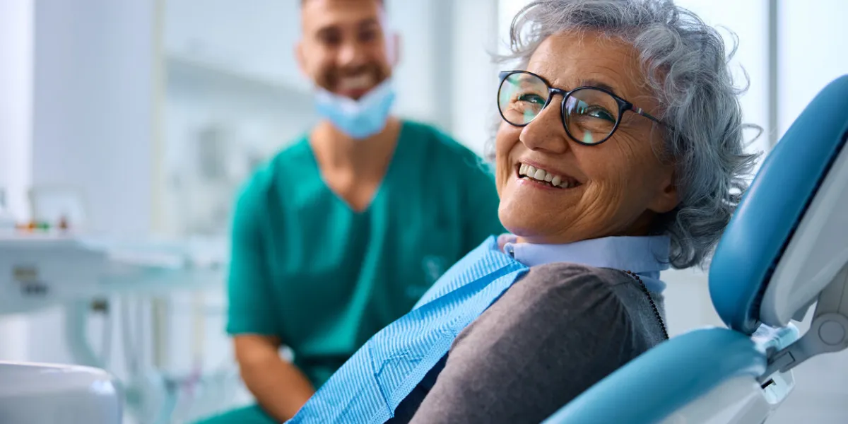 happy senior woman at dental clinic looking at camera her dentist is in the background
