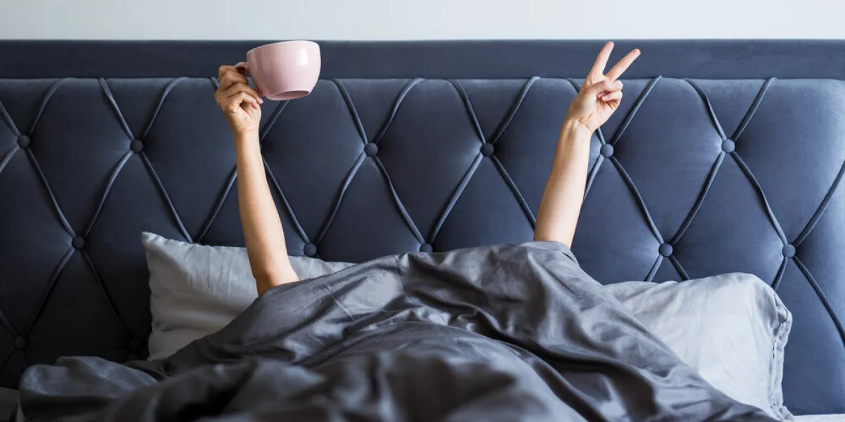 good morning concept - female hands with coffee mug and victory sign sticking out from the blanket in bedroom