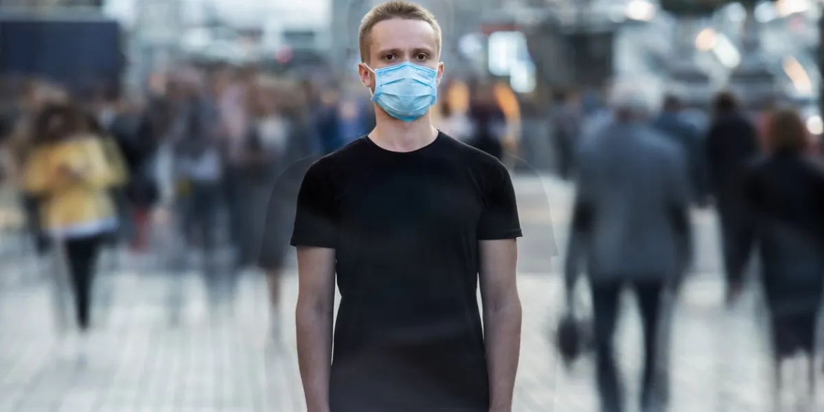 the young man with medical mask on his face stands on the urban street