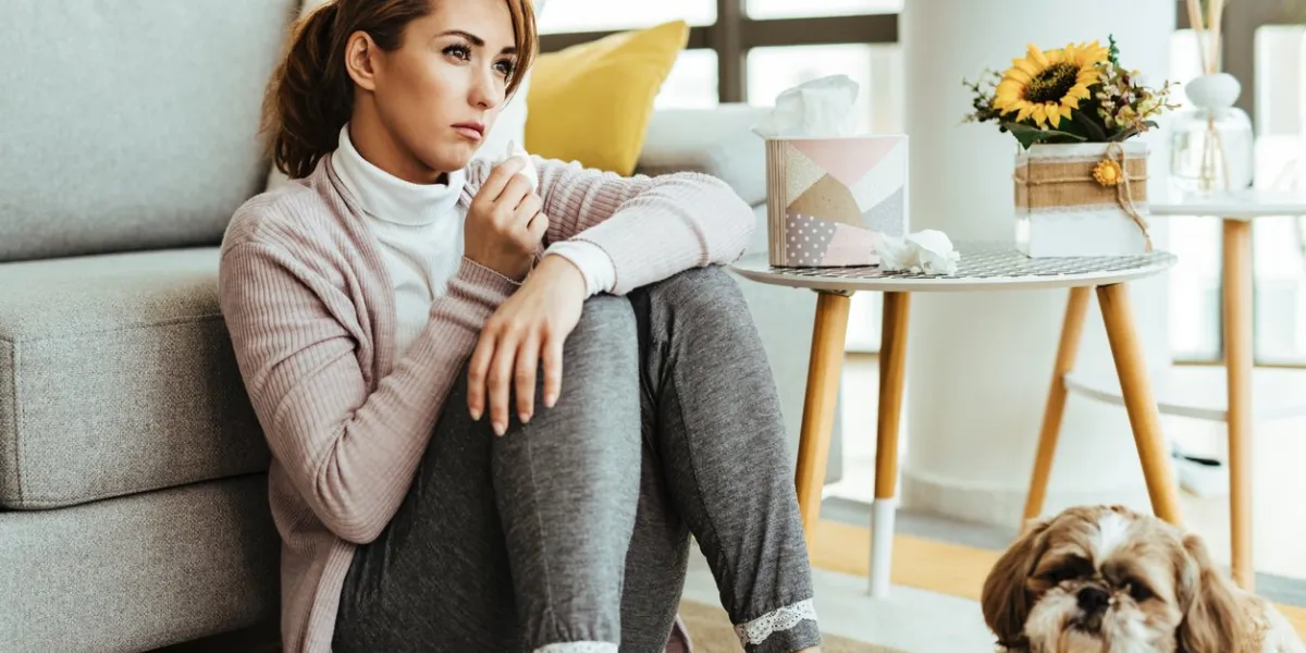 young woman feeling sad and using tissues while sitting on the floor at her home
