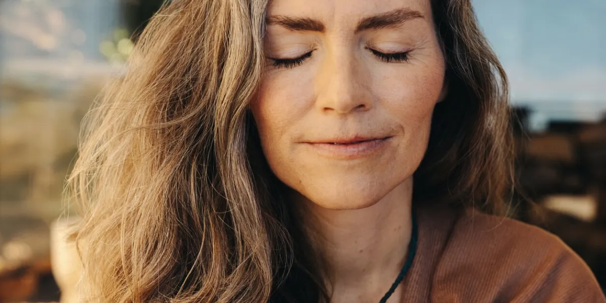 meditation and self-healing senior woman meditating with her eyes closed and with a crystal necklace around her neck mature woman practicing a holistic lifestyle at home