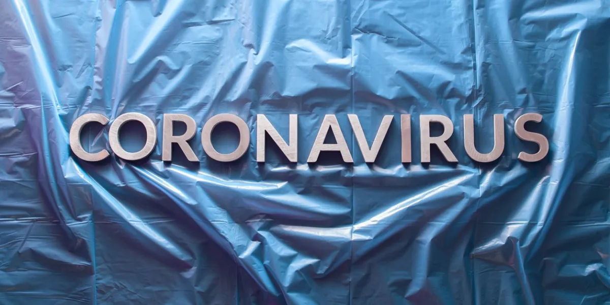 the word coronavirus laid with silver letters on crumpled blue plastic film - centered flat lay composition with dramatic light