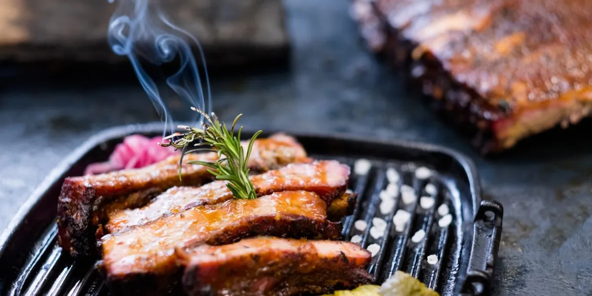 grill restaurant menu closeup of smoked pork ribs, served in griddle pan and decorated with burning rosemary twig