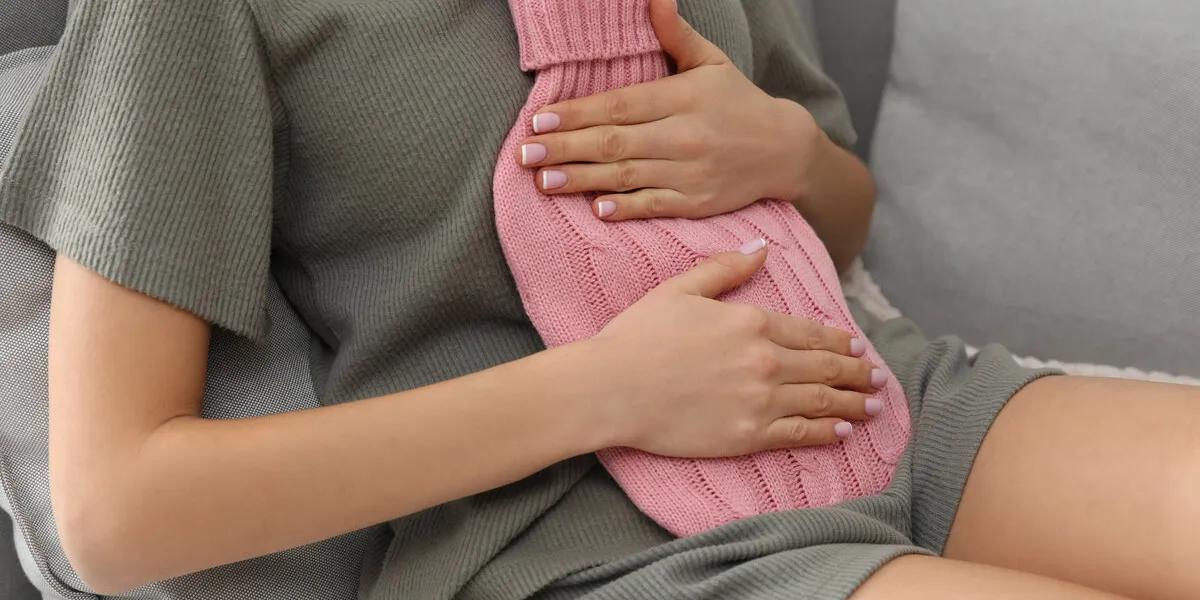 woman using hot water bottle to relieve menstrual pain on sofa at home, closeup