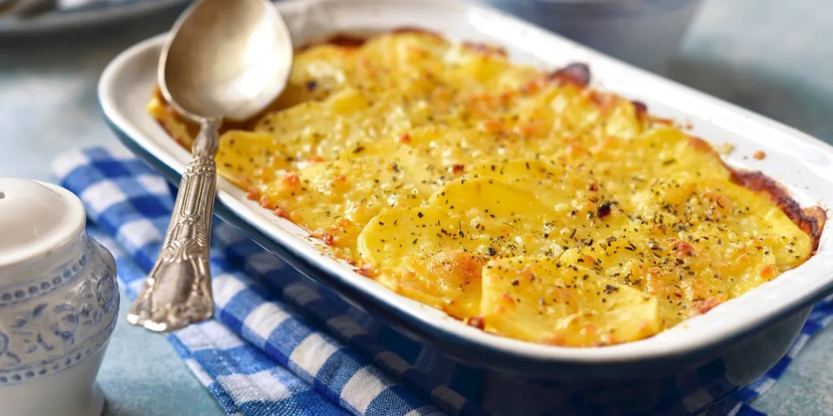 potato celery gratin with cheese in a baking diash on a light blue slate, stone or concrete background