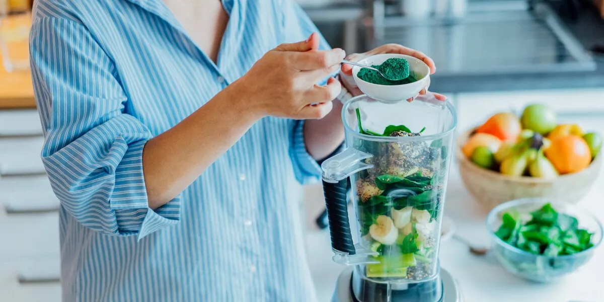 woman adding spirulina green powder during making green smoothie on the kitchen superfood supplement healthy detox vegan diet healthy dieting eating, weight loss program selective focus