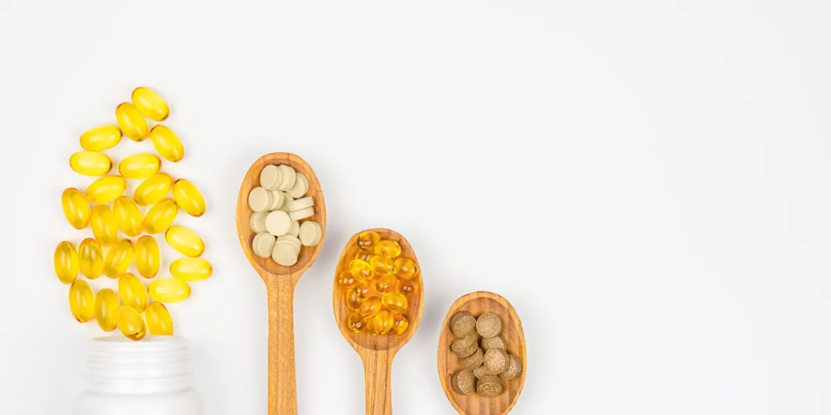 dietary supplements and vitamin pills in bottle and spoons on white background health care concept