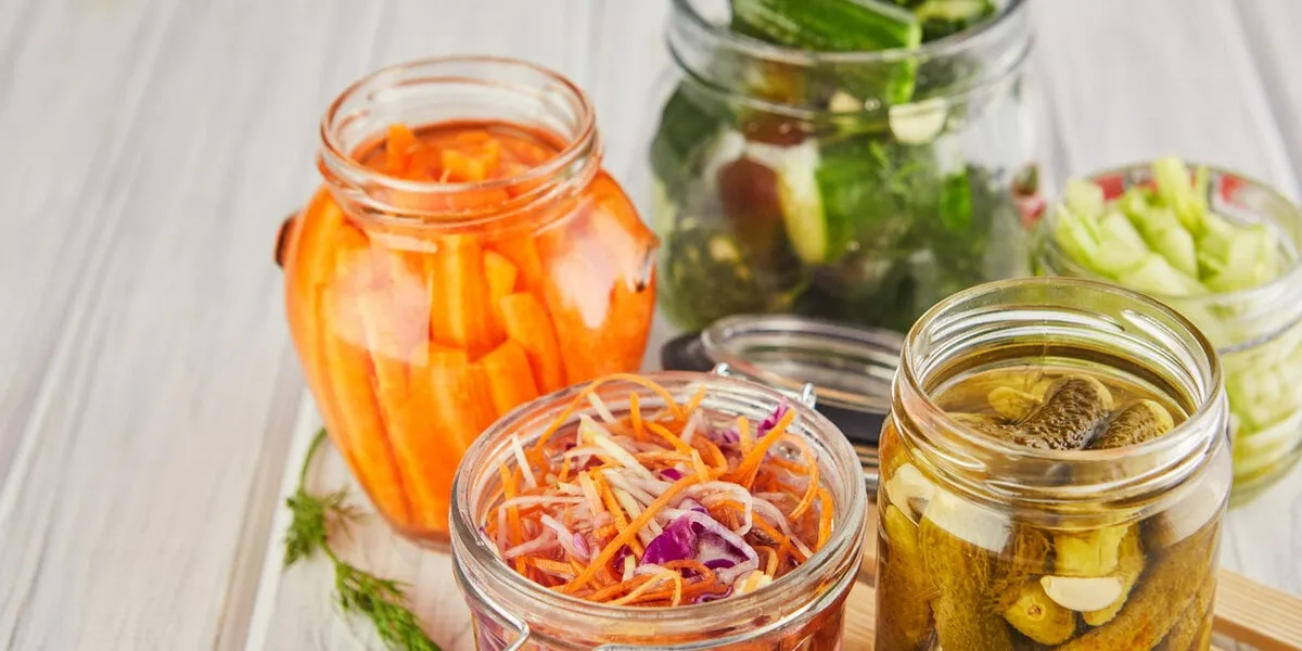 fermented preserved vegetarian food concept sour sauerkraut, pickled carrots, pickled cucumbers, pickled celery in glass jars on a white wooden kitchen table the concept of canned food copy space
