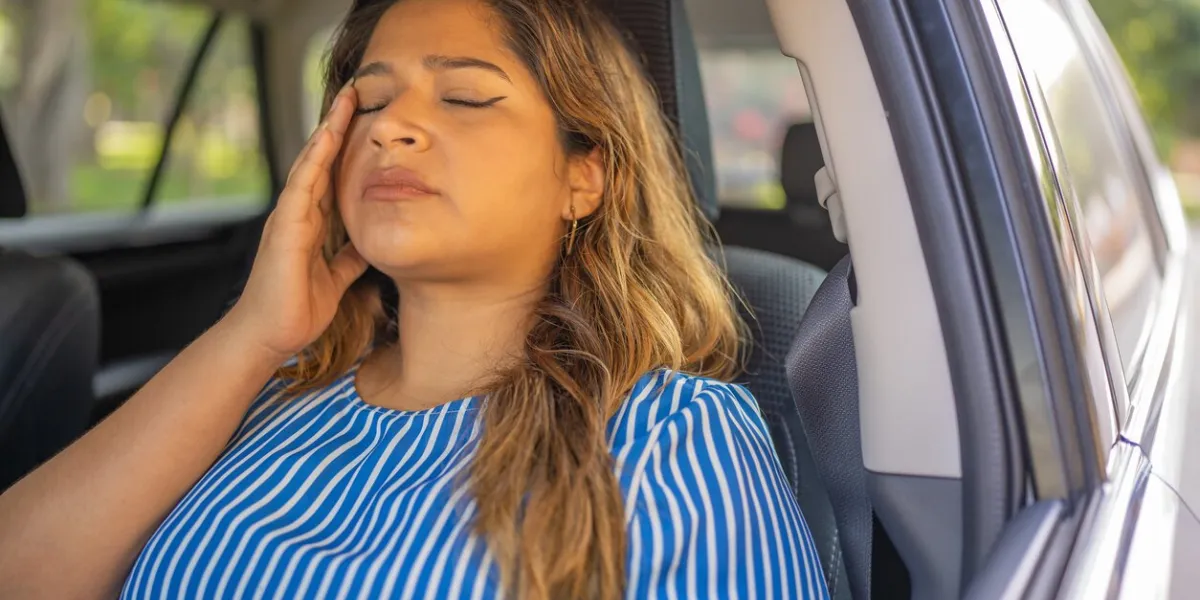 woman with migraine sitting in car, with hand on head