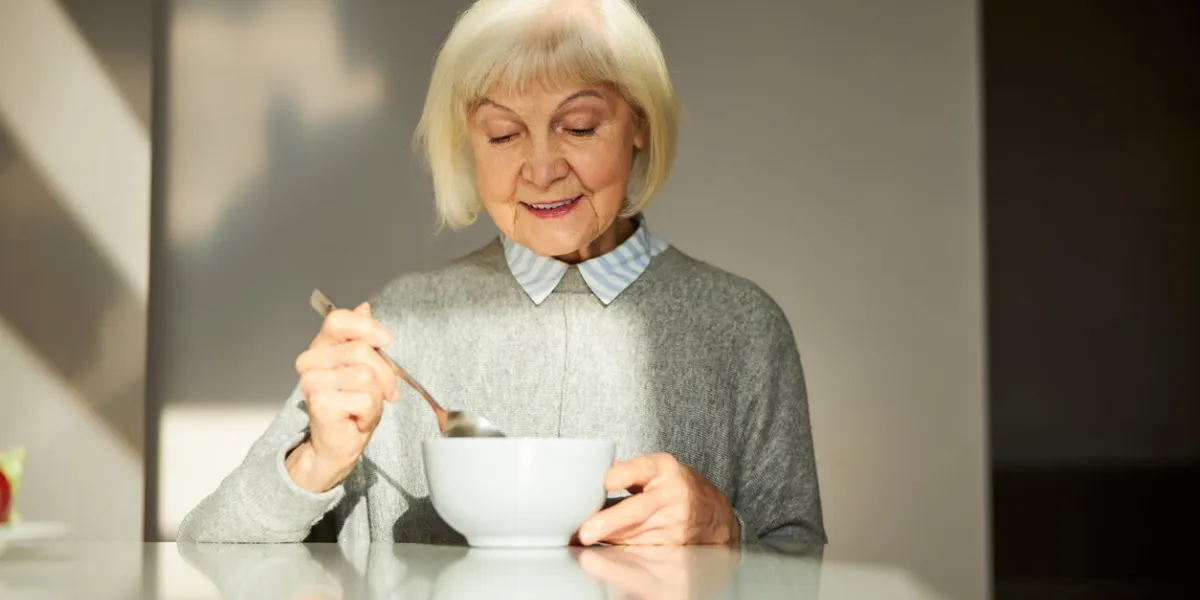 portrait of a pleasant smiling pleased female pensioner eating her oatmeal porridge in the morning