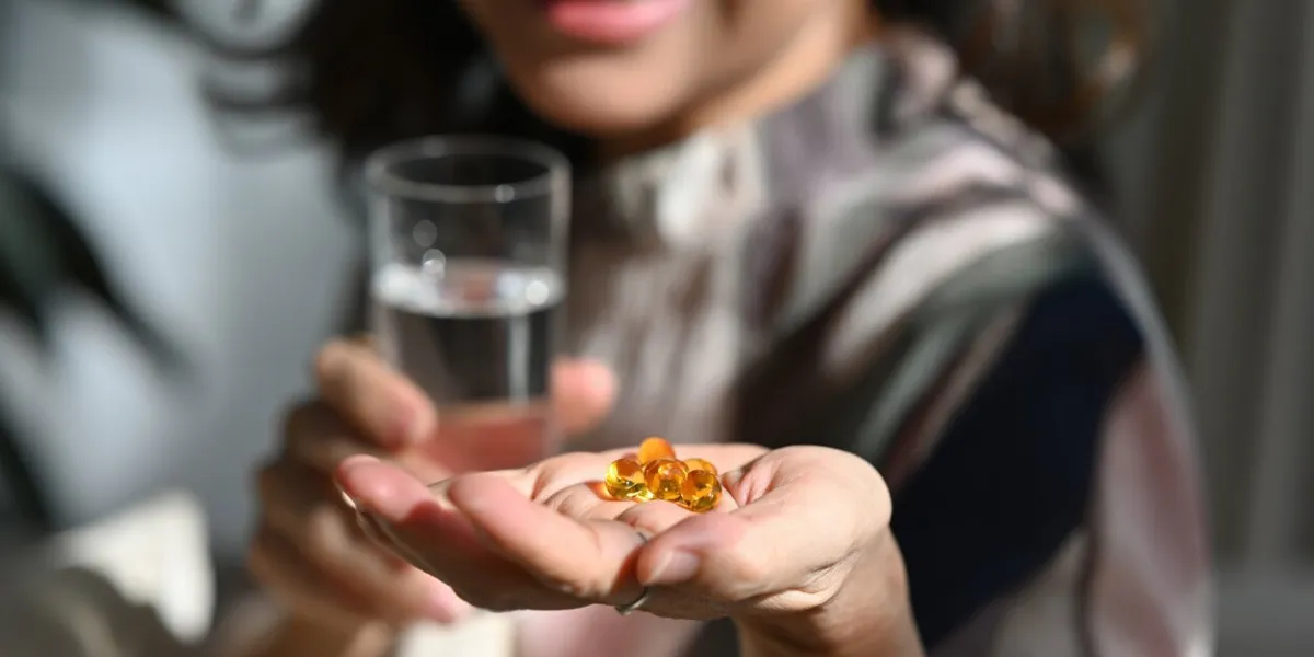 selective focus of wrinkled hands of a senior woman holding fish oil or omega-3 supplement capsule