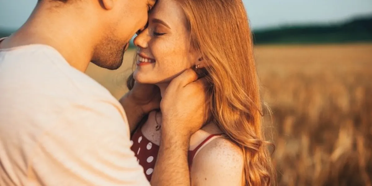 a couple touching foreheads being romantic and kissing while posing under sunlight with a blurry background love and relationships outdoors
