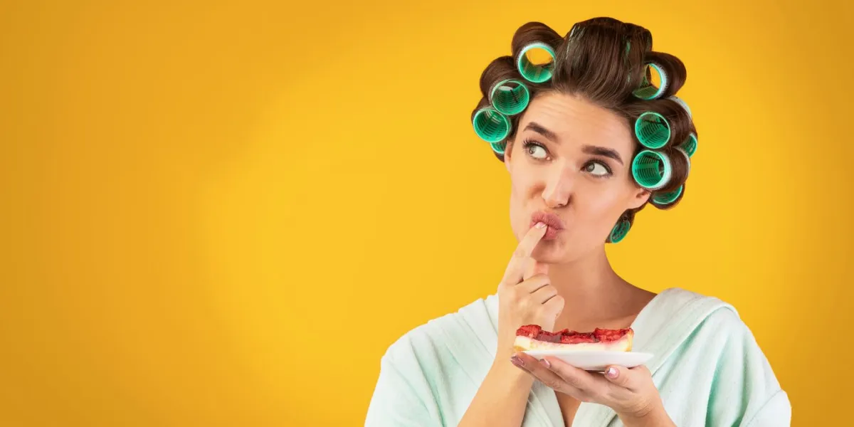 cheat meal concept hungry housewife tasting cake standing over yellow studio background panorama, free space for text