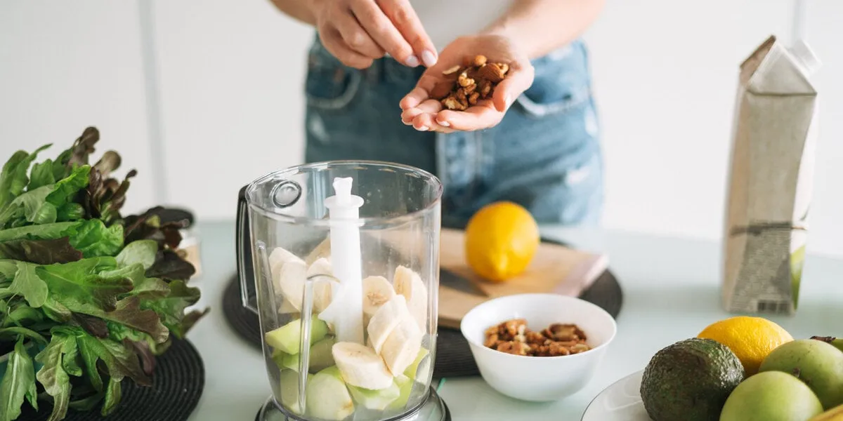 young slim woman in white t-shirt and blue jeans cooking smoothie with bananas healthy food in kitchen at home