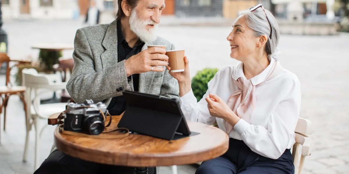 stylish aged couple relaxing together on cafe terrace and enjoying hot coffee lovely wife and husband using digital tablet and retro camera outdoors