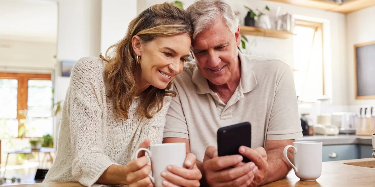 senior couple on smartphone reading online social media post, search holiday house website or retirement planning inspiration with home wifi happy elderly pension people with cellphone chat app