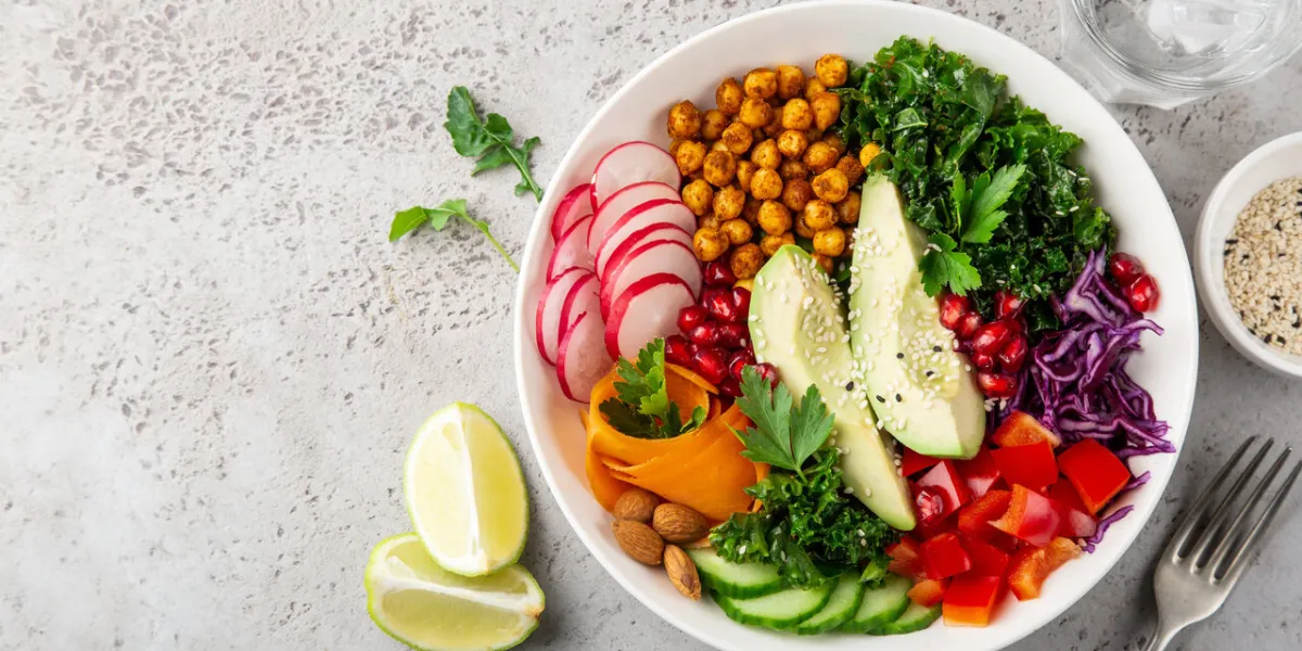 lunch bowl salad with avocado, roasted chickpeas, kale, cucumber, carrot, red cabbage, bell pepper and redish, healthy vegan food, top view, copy space