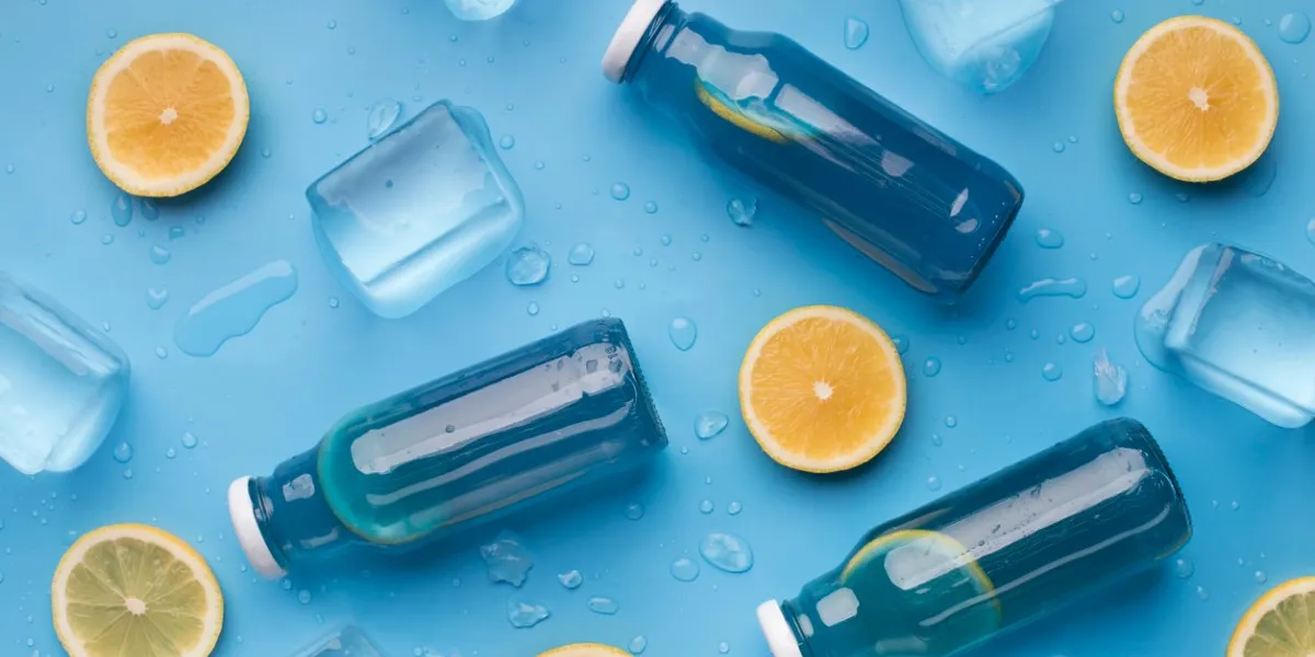 summer background with blue detox water, fresh lemons and ice cubes on blue