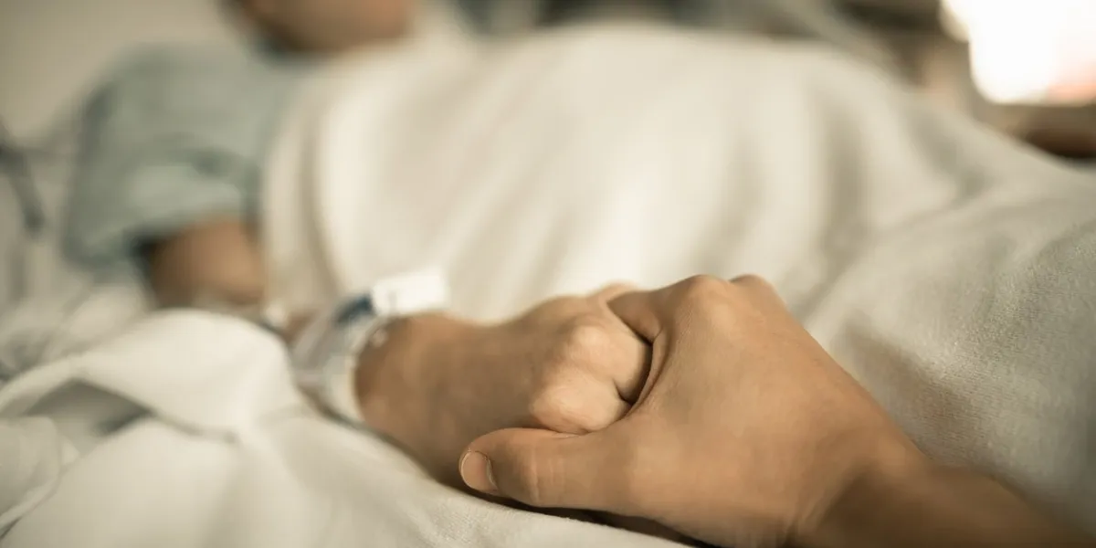 man holding hand, giving support and comfort to woman, loved one sick in hospital bed