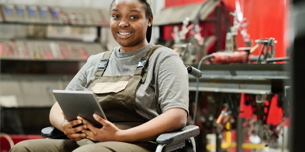 portrait of african american woman with disability sitting on wheelchair and smiling at camera while working online on tablet pc