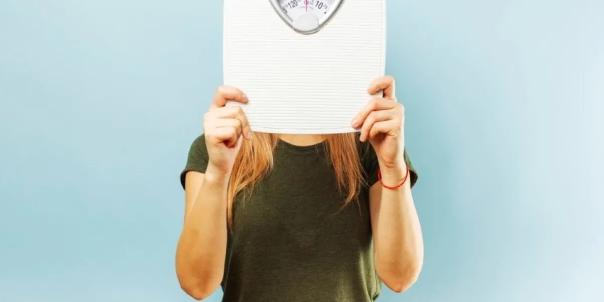 woman with weight scale young slim woman hiding her face behind weight scale on blue background