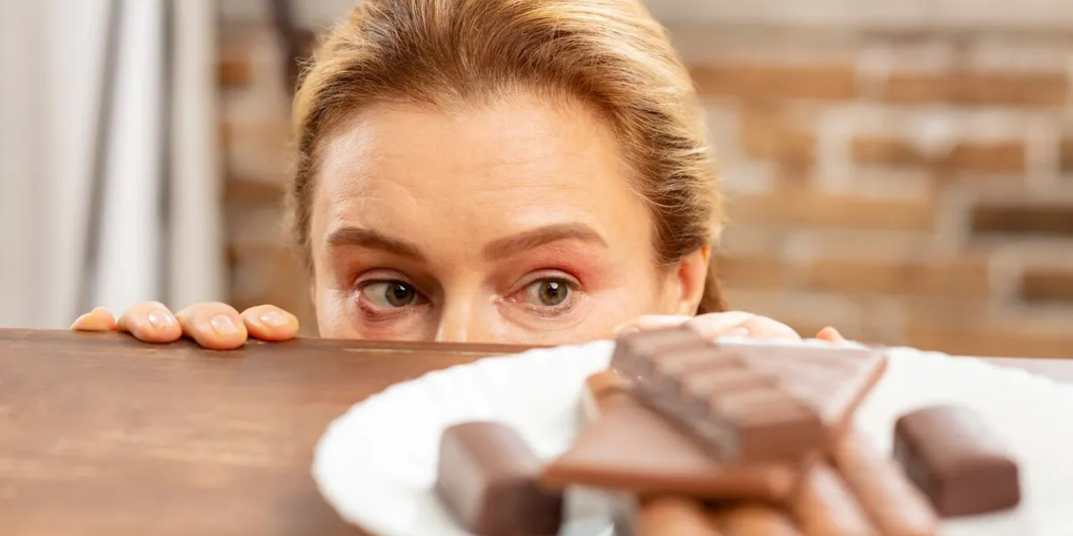 hiding and looking green-eyed mature woman hiding and looking at dark chocolate but feeling allergic