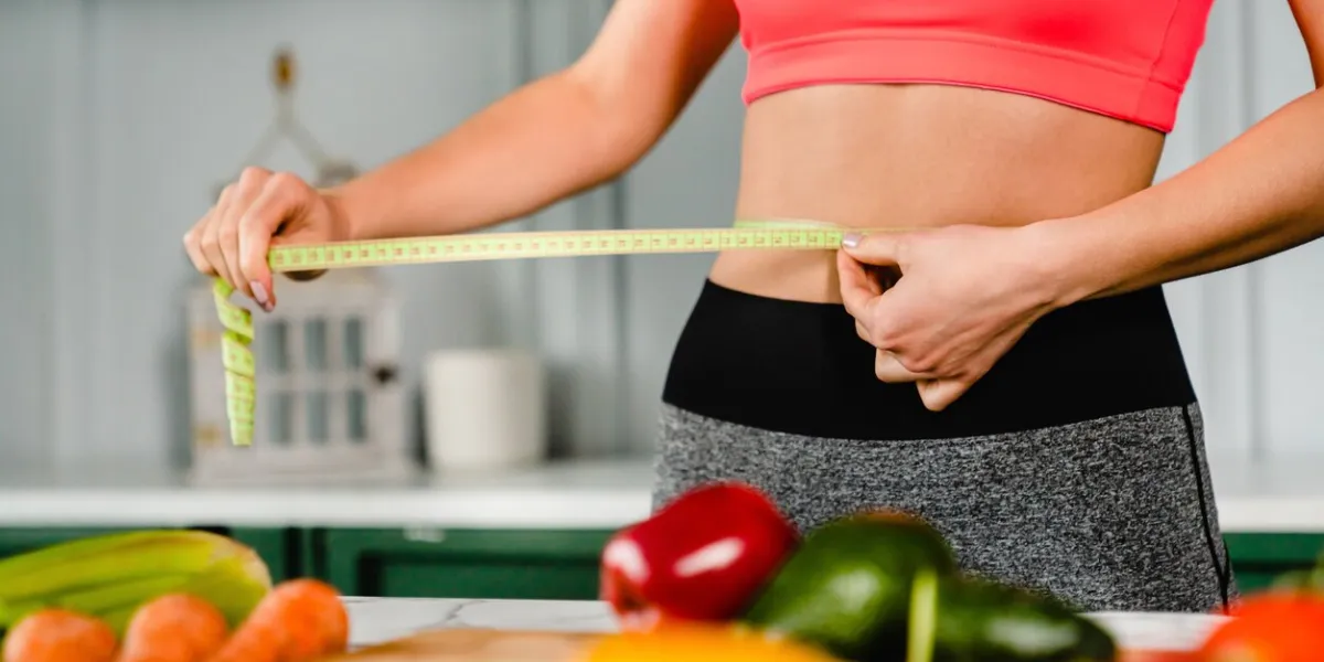 healthy fit girl measuring her waist with measuring tape in the kitchen