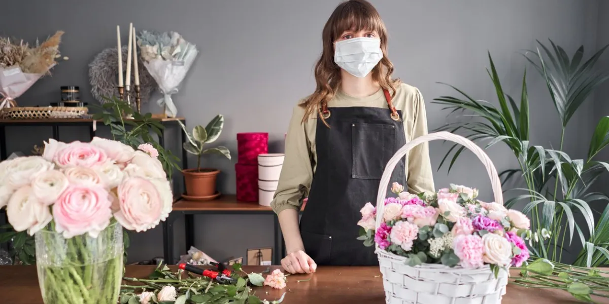florist woman in a medical mask for protection from coronavirus pandemic concept, working during an epidemic small flower shop flowers delivery
