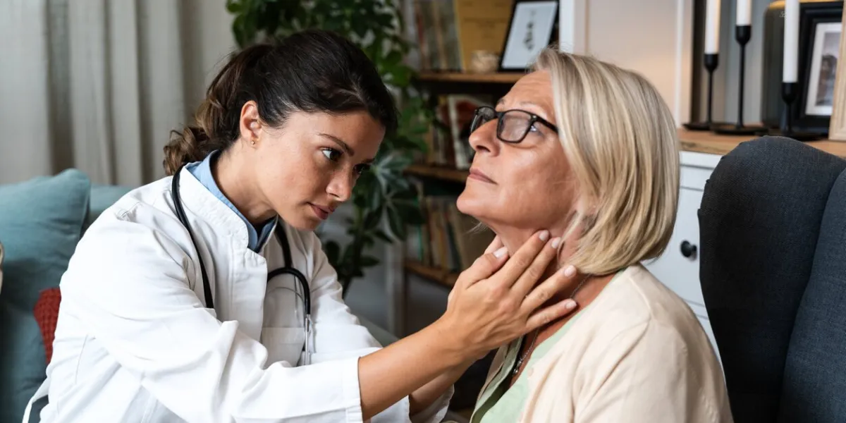 during a home visit to an elderly patient, a young endocrinologist doctor checks her thyroid gland by feeling her neck with her hands senior women endocrinology health care
