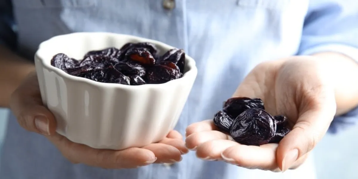 woman holding bowl and handful of dried plums, closeup healthy fruit