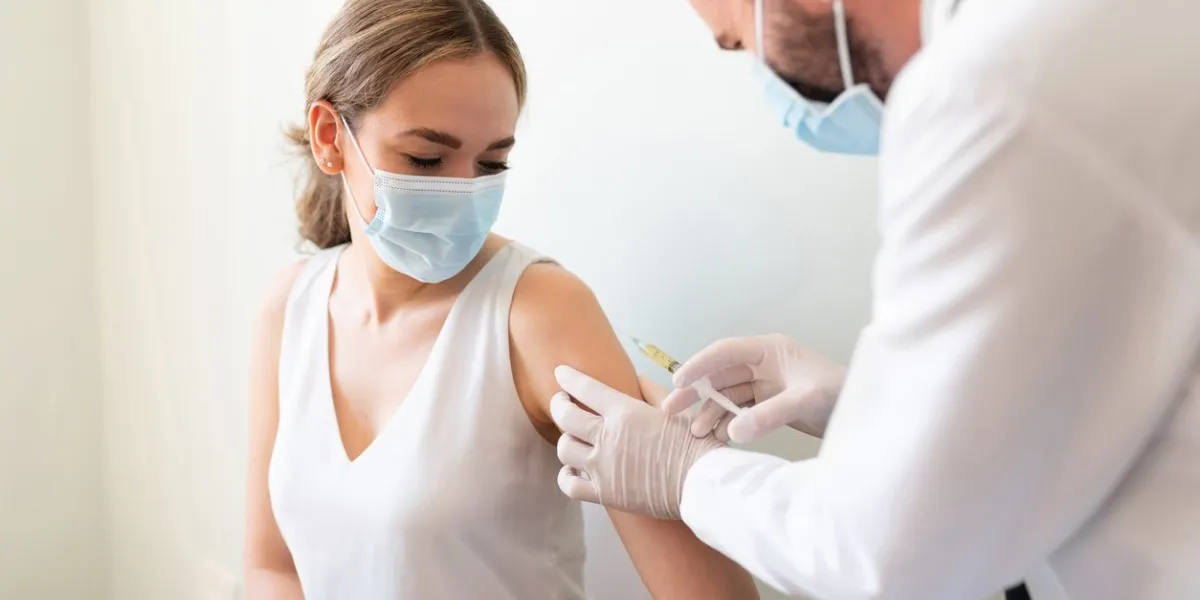 closeup of a nervous woman and her doctor wearing face masks and getting a vaccine shot in a doctor's office
