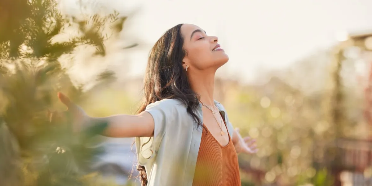 young latin woman with arms outstretched breathing in fresh air during sunrise at the balcony healthy girl enjoying nature while meditating during morning with open arms and closed eyes mindful woman enjoying morning ritual while relaxing in outdoor park