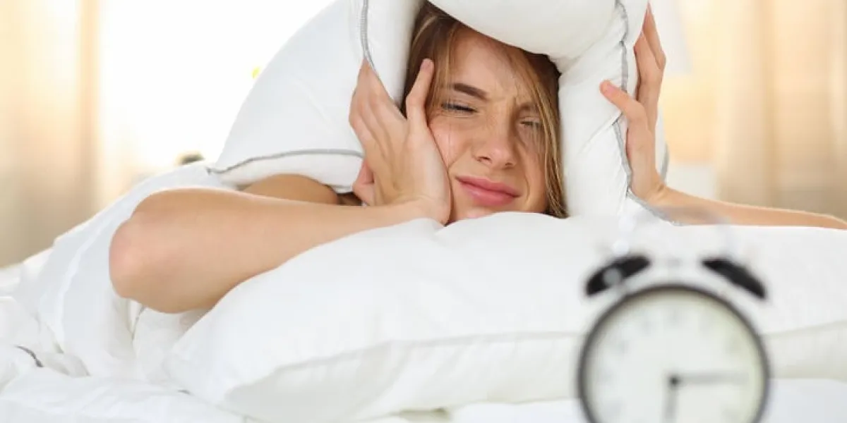 jeune belle blonde femme couchée dans son lit souffrant de son réveil couvrant la tête et les oreilles avec oreiller faire face désagréable tôt réveil, pas assez de sommeil, aller concept de travail