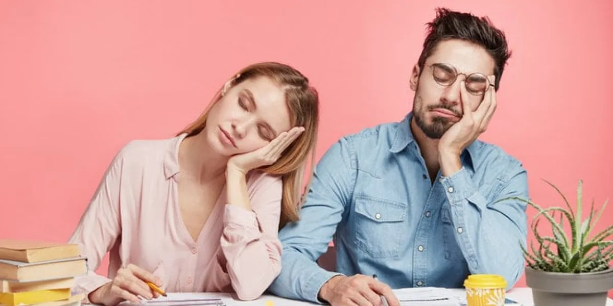 portrait tired crew of office workers sit at table, fall asleep after working long hours on preparing startup project, feel tiredness, isolated over pink background people and overworking concept