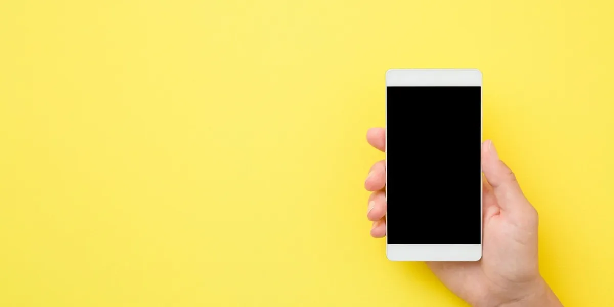 young woman hand holding smartphone on yellow background empty place for text on black screen close up top view