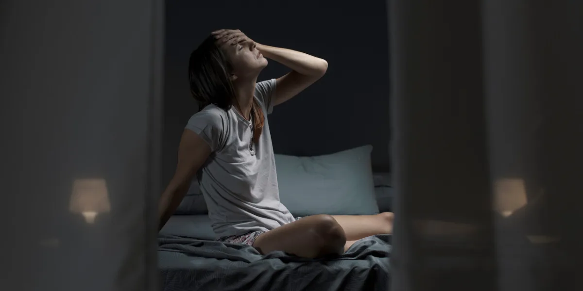 tired woman sitting in bed at night with open window, she is suffering from the heat and she is unable to sleep