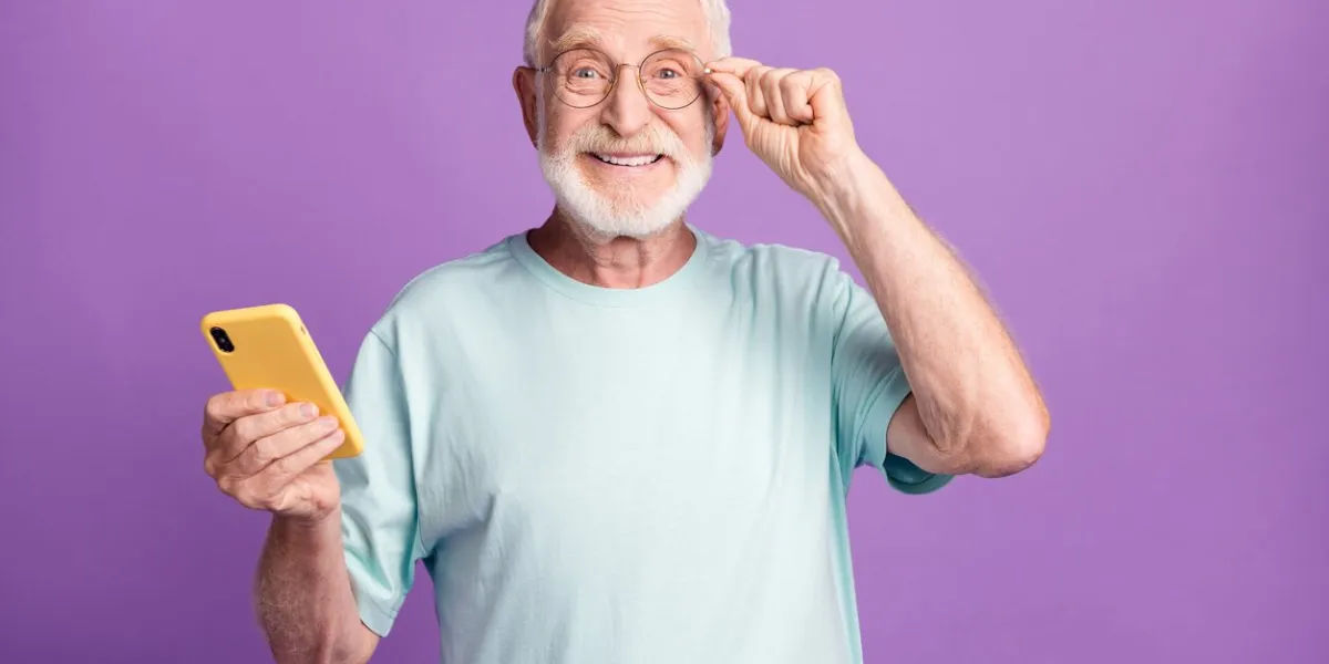 photo portrait of happy man touching glasses holding phone in one hand isolated on vivid violet colored background