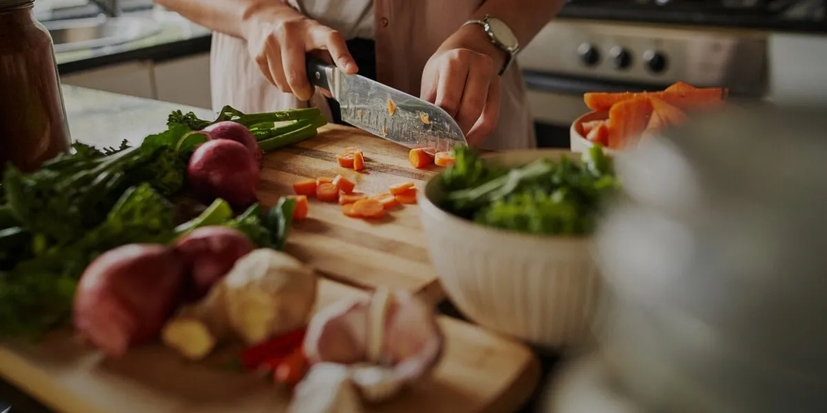 closeup of young female hands chopping fresh vegetables on chopping board while in modern kitchen - preparing a healthy meal to boost immune system and fight off coronavirus