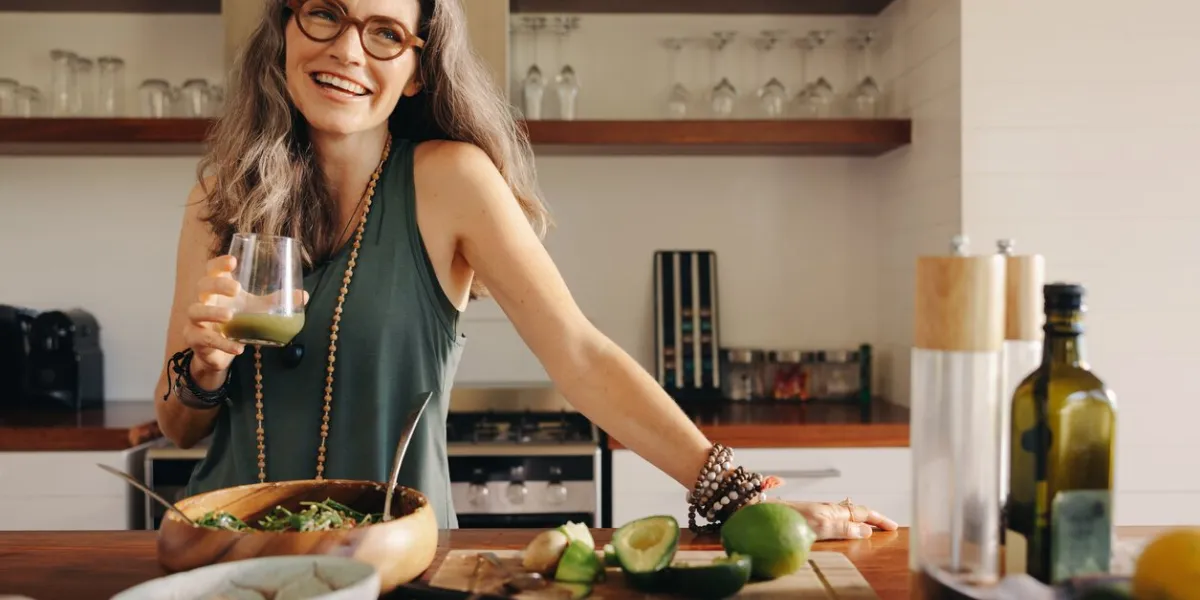 healthy senior woman smiling while holding some green juice in her kitchen mature woman serving herself wholesome vegan food at home happy woman taking care of her aging body with a plant-based diet