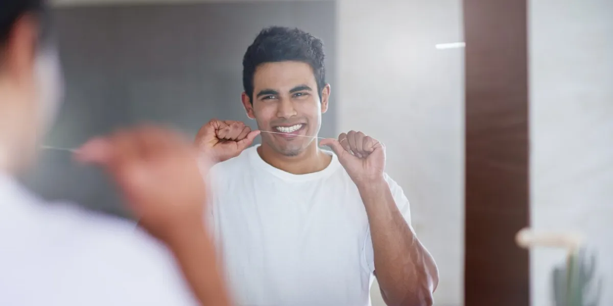 happy, mirror and man with floss in bathroom for dental hygiene, gum disease and oral care health, mouth and person in reflection after brushing teeth for wellness, cleaning and fresh breath in home