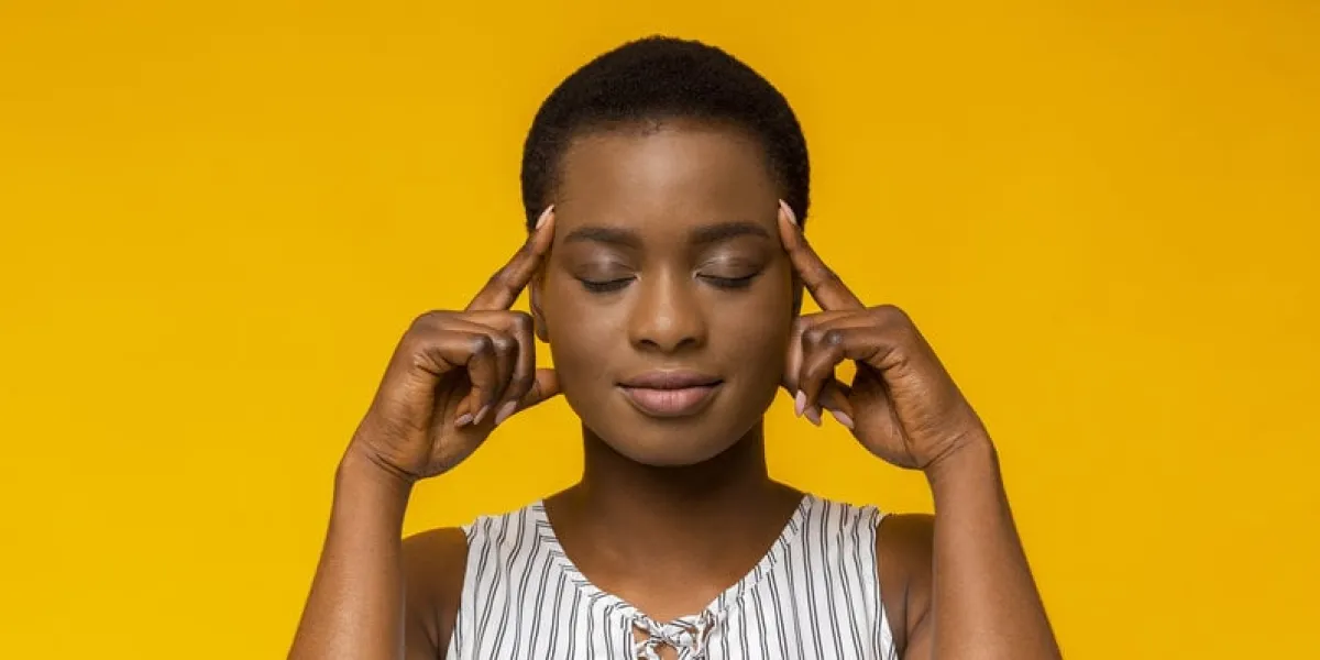 concentration afro girl holding fingers on temples, thinking hard, trying to concentrate, yellow studio background