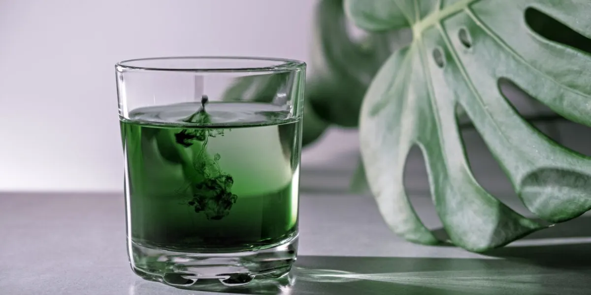 chlorophyll extract is poured in pure water in glass against a white grey background with green leaf liquid chlorophyll in a glass of water concept of superfood, healthy eating, detox and diet slow motion, close up, copy space