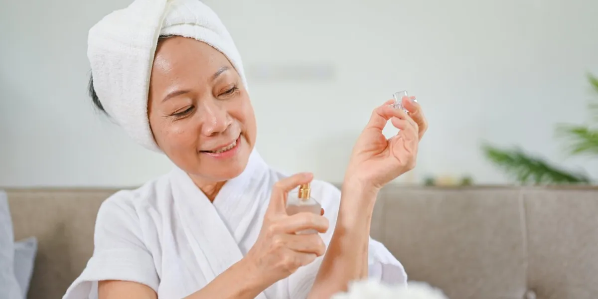 beautiful asian-aged woman in bathrobe applying perfume on her wrist after shower