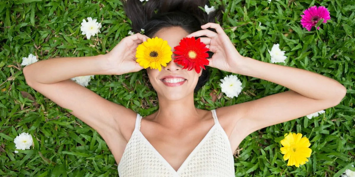 angle view of a woman holding gerbera flowers on her eyes while lying on the grass
