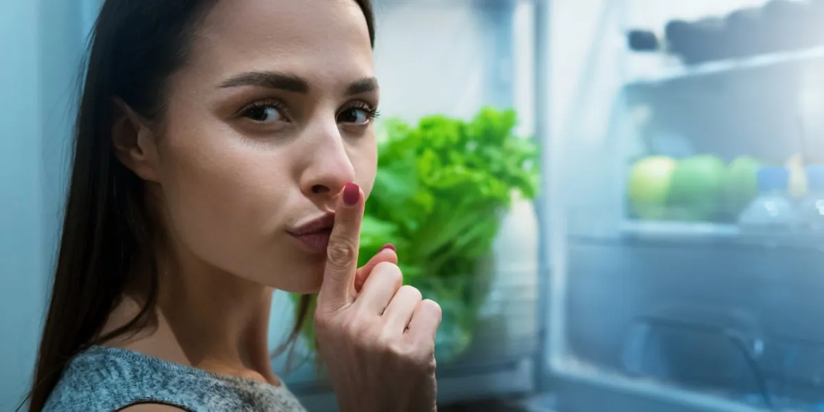 girl getting secretly to eat from fridge at night, asking to keep silent unhealthy eating concept