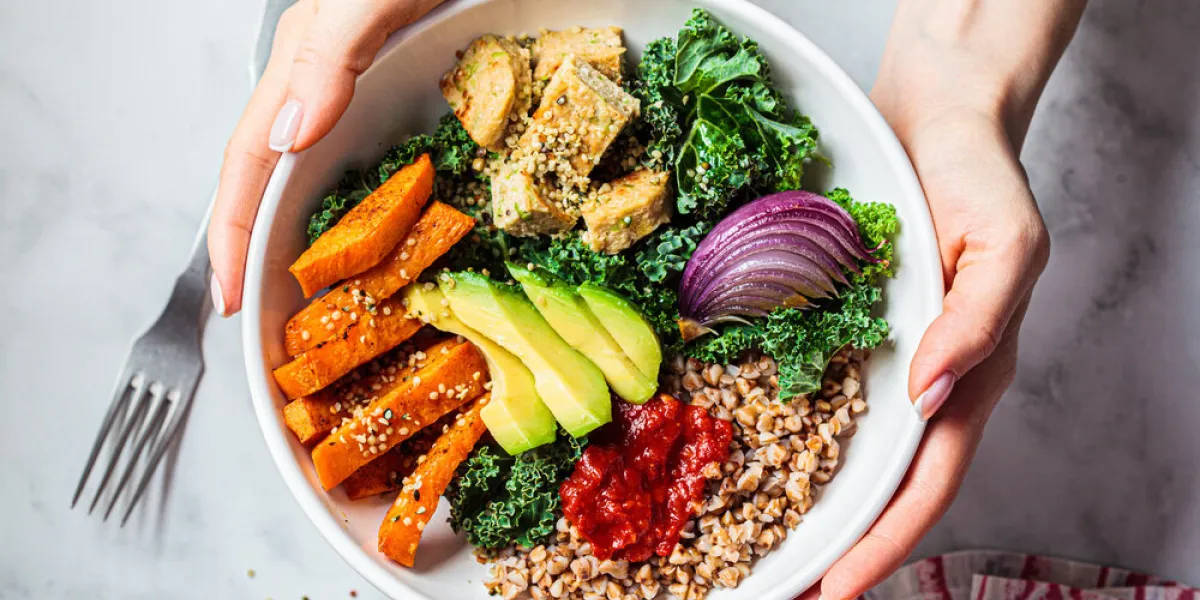 baked vegetables, avocado, tofu and buckwheat buddha bowl vegan lunch salad with kale, baked sweet potato, tofu, buckwheat and avocado in a white bowl vegan concept