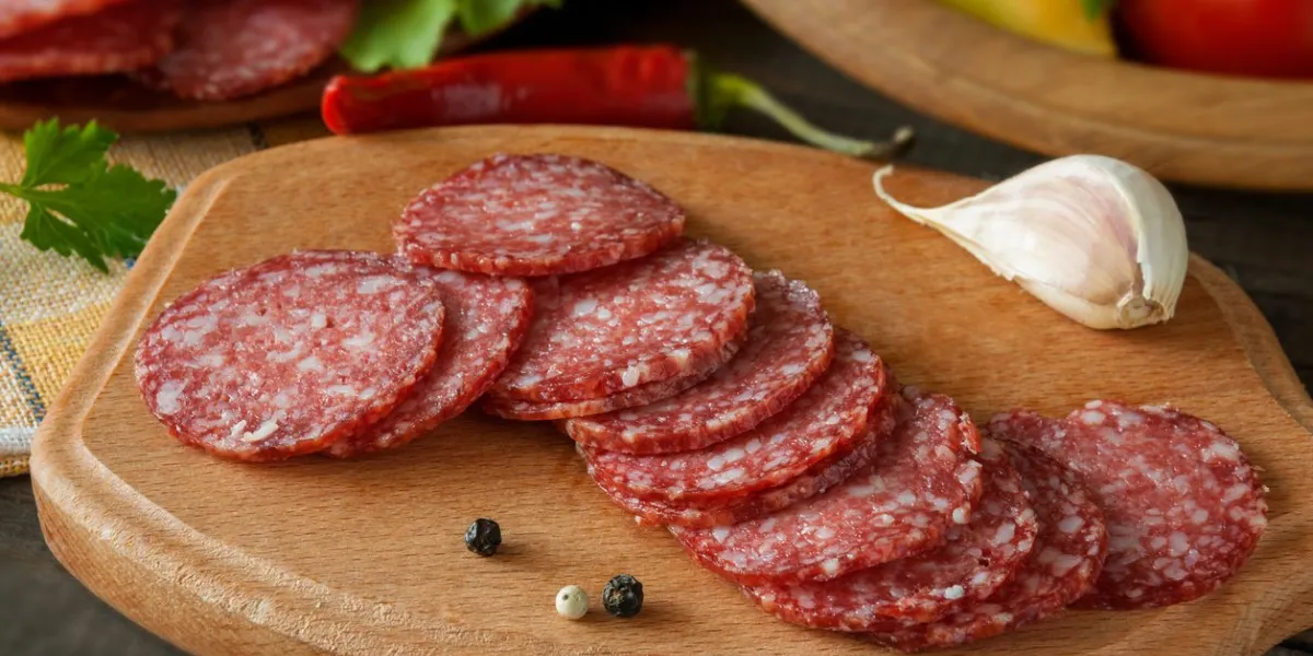 slices of salami with vegetables pepper and garlic on a cutting board on a wooden table