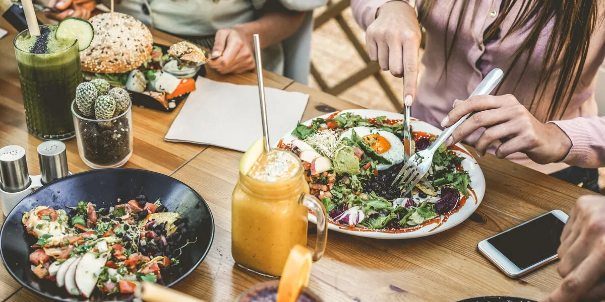 hands view of young people eating brunch and drinking smoothies bowl with ecological straws in plastic free restaurant - healthy lifestyle, food trends concept - focus on top fork dish