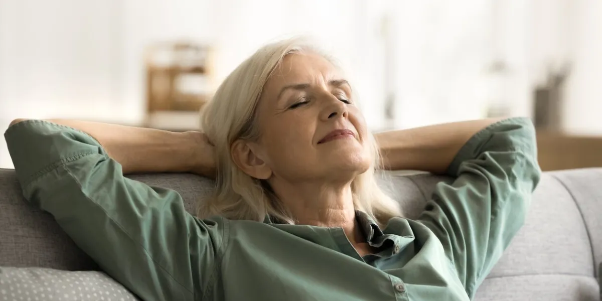 positive tranquil elderly woman relaxing on couch with closed eyes, smiling, stretching body, leaning on soft back with open elbows, enjoying leisure, calm lazy break at home, breathing fresh air