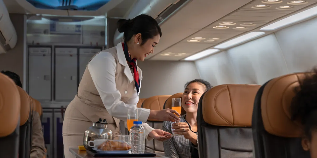air hostess or cabin crew working in airplane female flight attendant serving orange juice to businesswoman passenger on board airline transportation and tourism concept